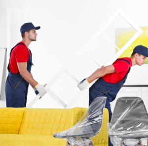 Möbel tragen Zwei Helfer tragen ein Möbelstück an einem gelben Sofa vorbei