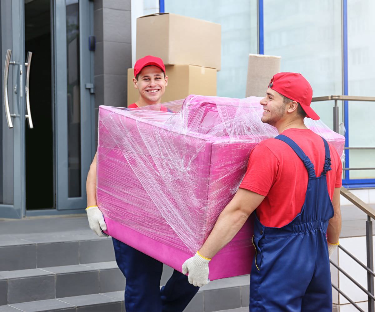 Zwei Umzugshelfer tragen ein in Folie gepacktes Möbelstück – Umzug von Meiningen nach Färöer