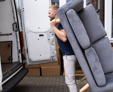 Möbellift Meiningen: Helfer tragen ein graues Sofa aus einem Transporter